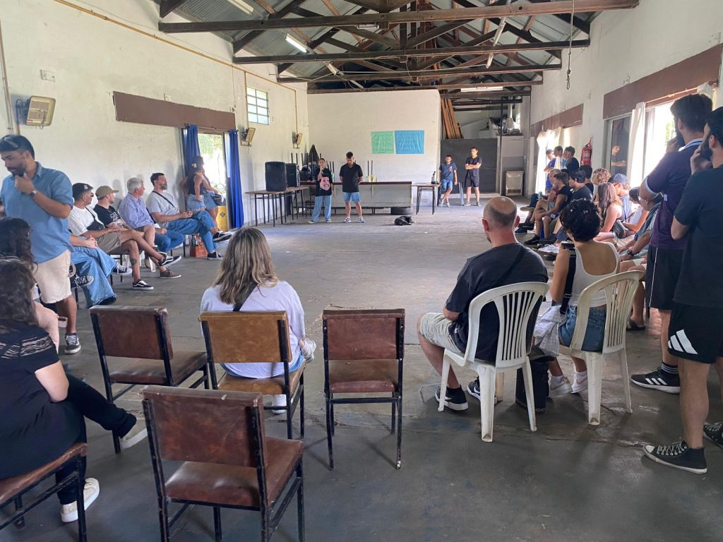 Asamblea del lanzamiento: sillas en círculo y compañeros escuchando.