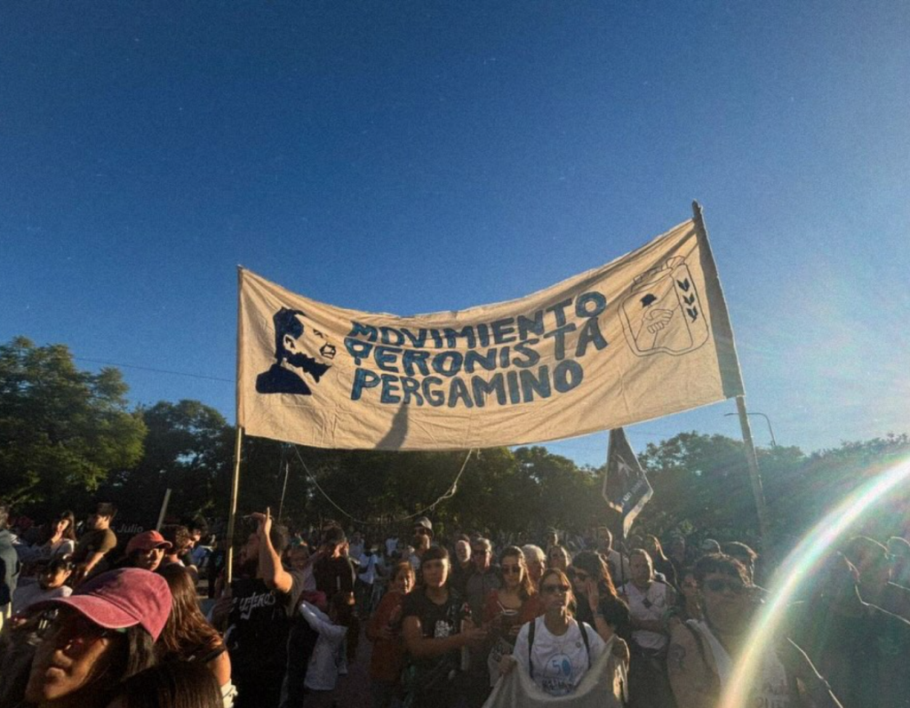 La bandera del Movimiento Peronista Pergamino flamea sobre la multitud, al anochecer.
