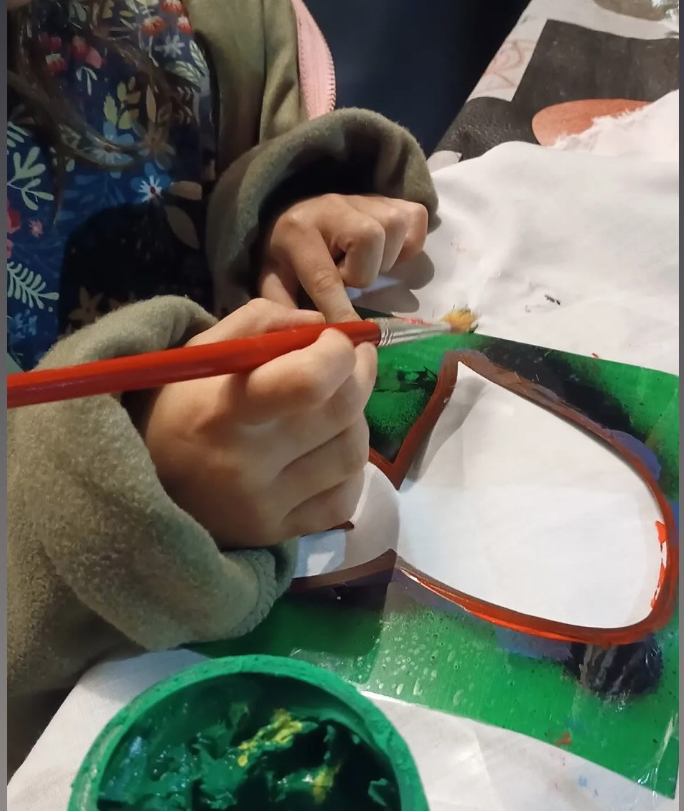Un chico pinta un pañuelo blanco con témpera verde.