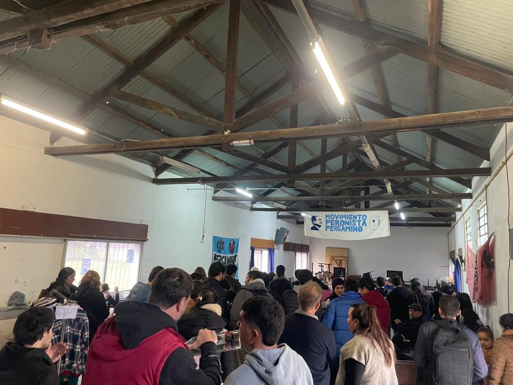 El salón lleno de gente durante la peña, con la bandera del espacio al fondo.