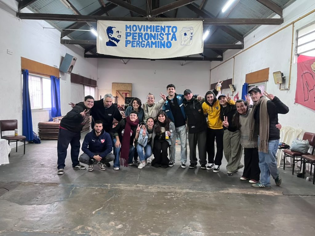 Militantes posan en grupo bajo la bandera del Movimiento Peronista Pergamino, en el salón.