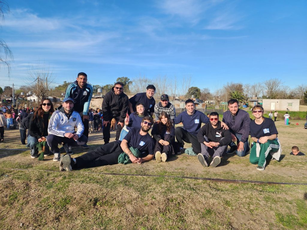 Militantes del espacio posan sentados en el pasto del predio, con vecinos y juegos al fondo.