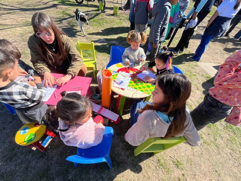 Chicos pintan y dibujan en mesitas de plástico, acompañados por dos militantes.