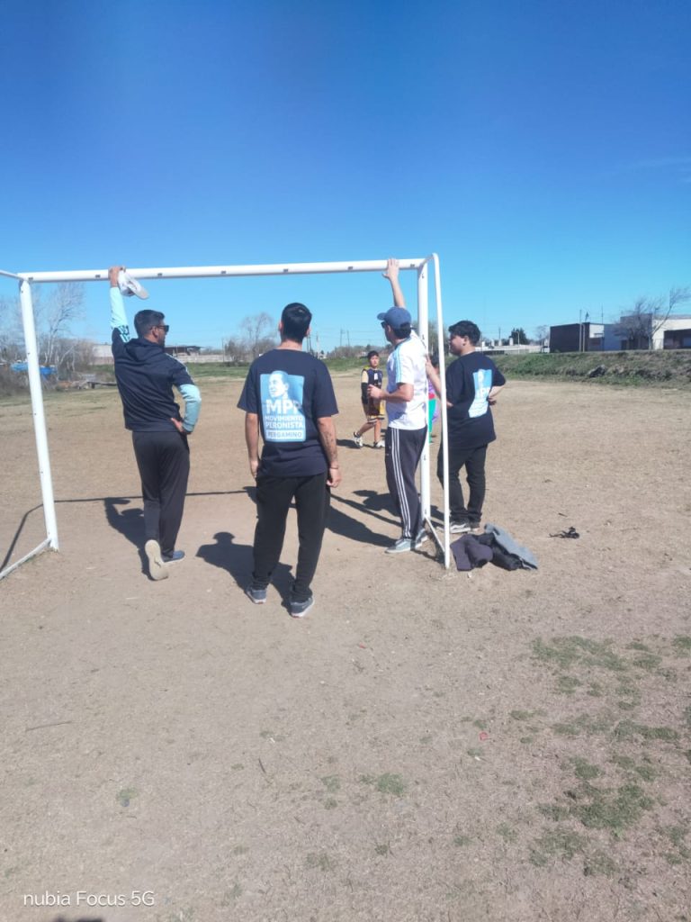Militantes y chicos juegan al fútbol en la cancha de tierra del barrio.